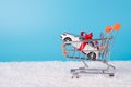 Winter sale concept. Close up photo of toy mini white car in miniature shopping cart on snow isolated on blue background Royalty Free Stock Photo