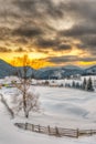 A winter scene featuring a rustic red barn surrounded fence and a cluster of evergreen at sunset Royalty Free Stock Photo