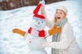 Winter scene with happy people on white snow background. Winter day. Girl playing with snowman in winter park. Royalty Free Stock Photo