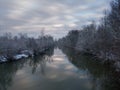 Winter scene with river and snow covered riverbanks and trees, clouds reflecting in calm water Royalty Free Stock Photo