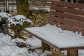 Winter scene of wooden park bench covered with snow next to snow Royalty Free Stock Photo