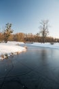 Winter scenery with frozen river with small bridge above, trees, snow and clear sky