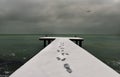 Winter sea landscape. Pier in the snow and footprints of a man,