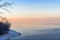 Winter sea at sunset, clear evening. Orange and blue sky, shore covered snow, bare trees. Royalty Free Stock Photo