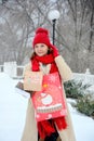 Winter shopping. A young woman in a red scarf and hat stands with gift bags on the street in winter Royalty Free Stock Photo