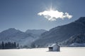 Winter shot of a barn in the snowy field, mountains in the background and sunbeams behind