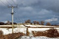 Winter shot of a field covered with snow and a power pole line under the gloomy sky Royalty Free Stock Photo