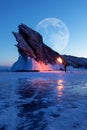 Winter Siberian landscape. Lake baikal, silhouette of a man with a torch on the background of the rock and the moon. Lake Baikal.