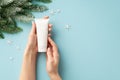 Winter skin care concept. First person top view photo of young woman`s hands holding white tube without label snowflakes and pine