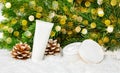 Set of winter skin care cosmetic products in snow under Christmas tree with pine cones and bokeh lights. Face cream jar and hand