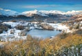Winter snow across the landscape of the Lake District with a tarn and blue skies