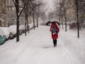 Winter. Snowing. A young girl in a red coat walks under an umbrella