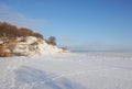 Winter snowy coastal landscape on a sunny day. Frozen river. Clear sky. Open space. Hill with trees