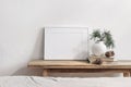 Winter still life. Horizontal white frame mockup on vintage wooden bench, table. Modern white ceramic vase with pine