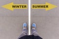 Winter and summer text arrows on asphalt ground, feet and shoes