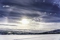 Winter Sun halo is above wild subarctic Scandinavian Mountains, frozen lake below, very cold day with clear blue sky, some clouds Royalty Free Stock Photo