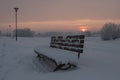 Winter sunset in a huge park with bench covered with snow