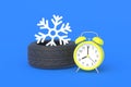 Winter tire near alarm clock and snowflake. Time, speed of car wheel replacement