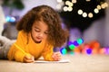 Thoughtful african little girl writing letter to Santa near Xmas tree