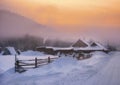 Winter village landscape, farm and wooden houses in the countryside, fog at sunset in the mountains Royalty Free Stock Photo