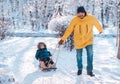 Winter walk: Father pulling sledge with toddler son in snowy day. Dad and kid enjoy ride and have fun. Focus on father face Royalty Free Stock Photo