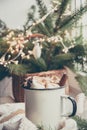 Winter warming mug of chocolate with marshmallow on windowsill with Christmas tree decor