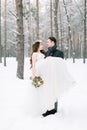 Winter wedding couple, bride and groom at their winter wedding day. Handsome groom holds her bride on hands
