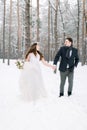Winter wedding in a snowy forest, lovely couple holding hands, looking each other, walking outdoors in winter forest Royalty Free Stock Photo