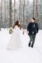 Winter wedding in a snowy forest, lovely couple holding hands, looking each other, walking outdoors in winter forest Royalty Free Stock Photo