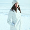 Winter weekend at the seaside concept. Emotive portrait of fashionable model in white coat and beret looking at camera. Sunny Royalty Free Stock Photo