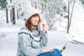 Winter woman portrait with a cup of tea in her hands siting in in snow-covered forest. Copy, empty space for text