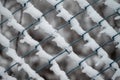 Wire mesh chain-link fence blanketed in snow illuminated by the sun with a bare tree in the backdrop Royalty Free Stock Photo