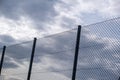 Wire mesh fence on cloudy sky background, low angle view. Metallic barrier, safety security concept Royalty Free Stock Photo