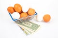 A wire shopping basket filled with white and brown eggs, placed beside rolled dollar bills and an egg, on a reflective white Royalty Free Stock Photo