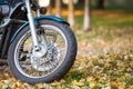 Wire-spoked wheel of a classic motorcycle standing on yellow leaves in autumn park, copy space