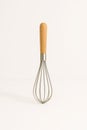 Wire whisk with wooden handle standing upright on white surface casting soft long shadow minimal kitchen tool concept for baking Royalty Free Stock Photo