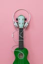 The wire from the white headphones entangles the neck of the ukulele.