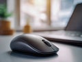 Wireless computer mouse placed on a desk surface with a blurred laptop and warm natural light streaming through a window in the Royalty Free Stock Photo