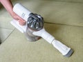 Wireless vacuum cleaner used on sofa in room. Housework with new upright hoover and nozzle. Person holds modern white vacuum