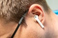 A wireless white small earpiece earphone in the ear of a man in black glasses close-up from the side. Horizontal