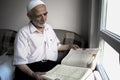 Wise old muslim man wearing taqiyah reads Turkish translation of Quran in passion