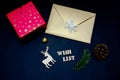 Wish list wooden letters on black background with Christmas decorations. Golden envelope and red gift box on dark