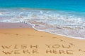 WISH YOU WERE HERE insctiption on wet beach sand with the turquoise sea on background Royalty Free Stock Photo