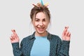 Wishful young woman smiling broadly, raises fingers crossed, makes desirable wish, wears casual outfit, posing on white wall. Royalty Free Stock Photo