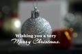 Wishing you a very Merry Christmas. Christmas card and greeting with white Christmas ball ornament closeup on blur decoration.