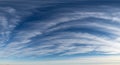 Wispy cirrus clouds stretch across a vast blue sky, creating delicate, sweeping