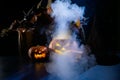 Witch casts a spell on a steaming pumpkin in the dark on Halloween