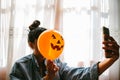 Witch holding a pumpkin balloon with her hand, covering her face and taking a photo with mobile phone. Young woman celebrating Royalty Free Stock Photo