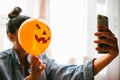 Witch holding a pumpkin balloon with her hand, covering her face and taking a photo. Young woman celebrating halloween. Helium Royalty Free Stock Photo