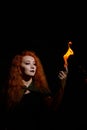 A witch with long curly hair holds a magic fire. Tongues of flame on the palms of a red-haired woman. Flaming eyes.